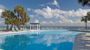Una piscina con sillas de descanso y palmeras, rodeada por una cerca y un muelle.