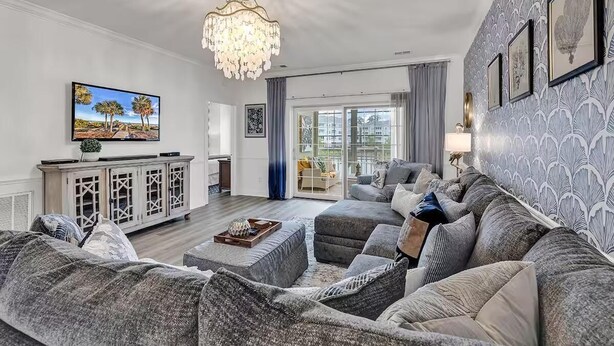 A modern living room with a large grey sofa, a television, and a chandelier.