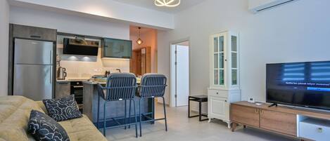 A modern living room with a sofa, a TV, and a kitchen area with a dining table and chairs.