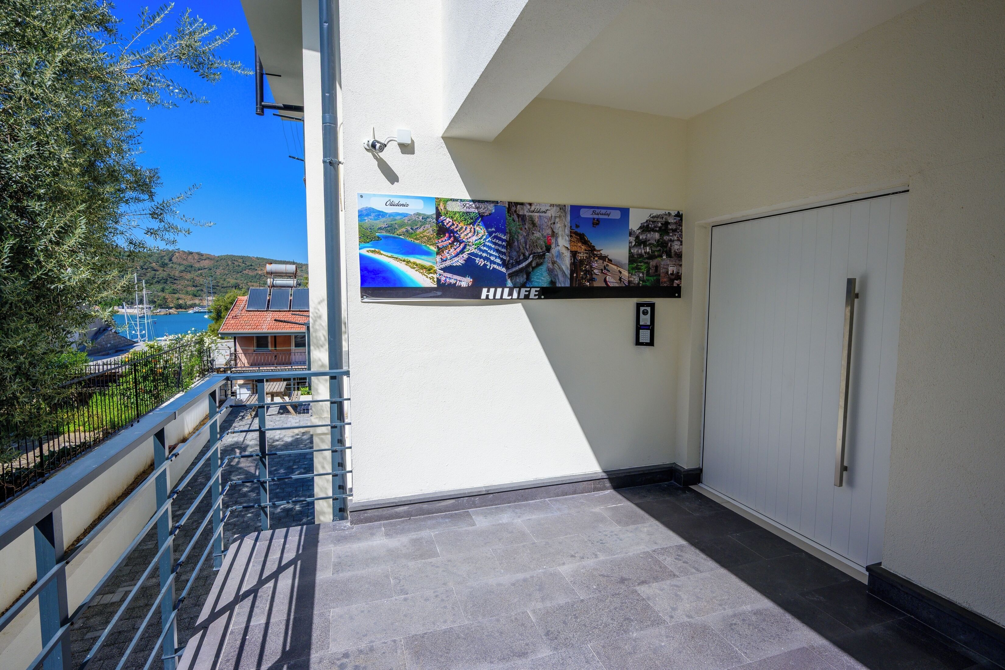 A hotel corridor with a view of the sea, a poster with various locations, and a door.