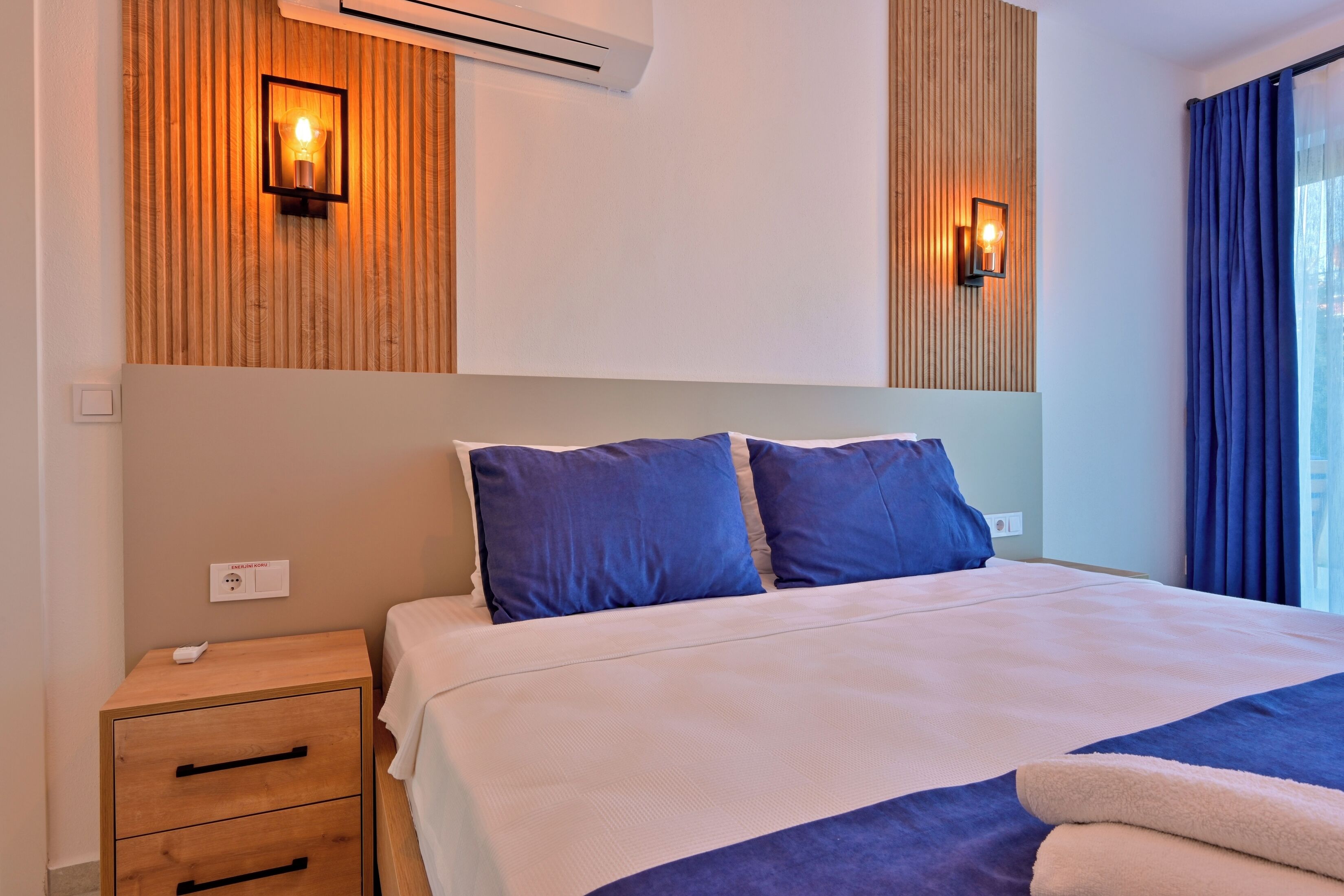 Una habitación de hotel con cama, mesitas de noche e iluminación en la pared.