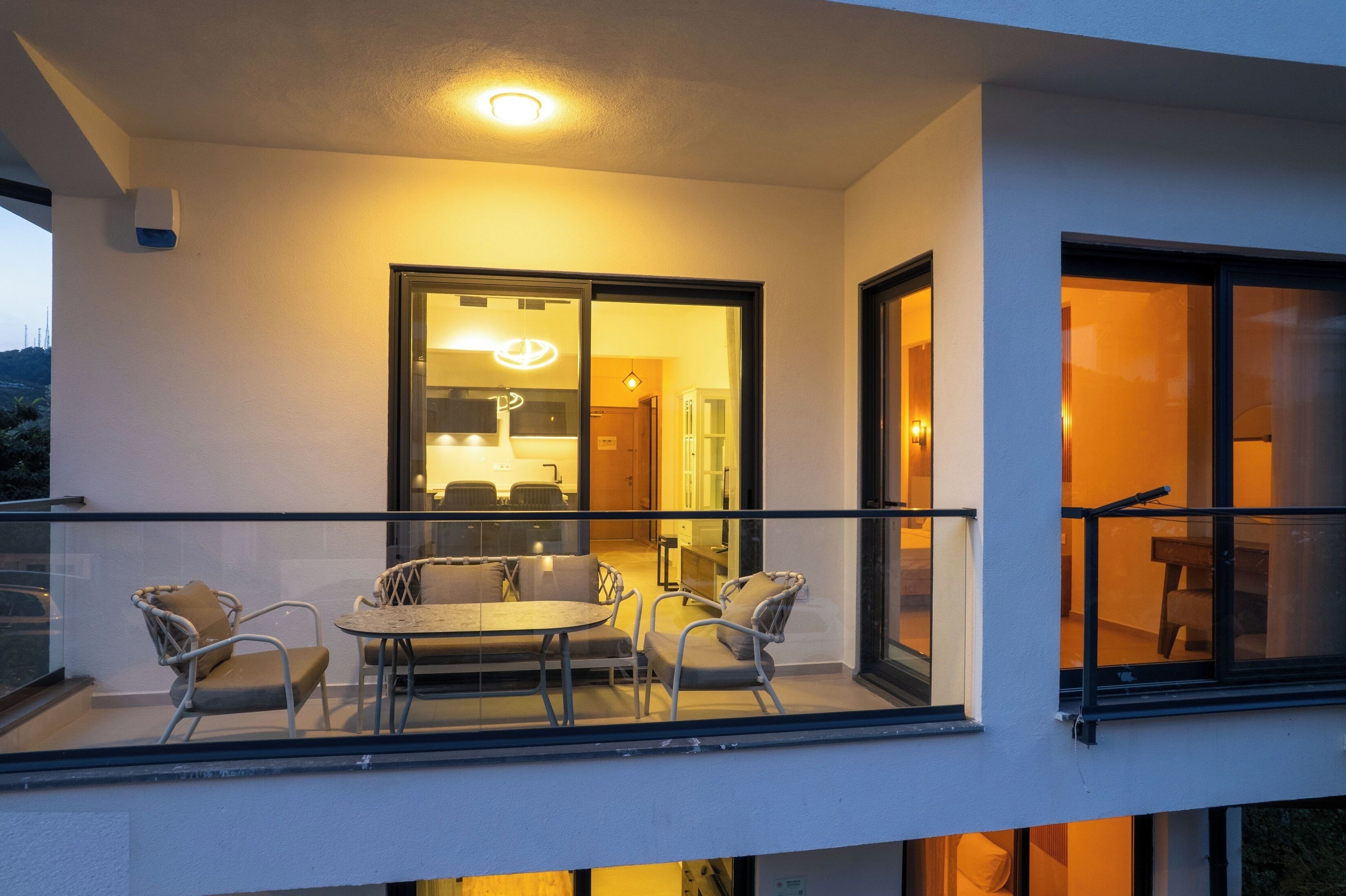 Un balcon avec une table et des chaises, une porte vitrée donnant sur un espace intérieur, et une vue sur l’extérieur.