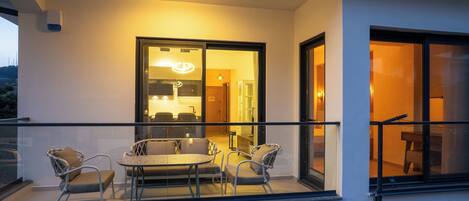 A balcony with a dining table and chairs, a glass door leading to an interior space, and a view of the outside.