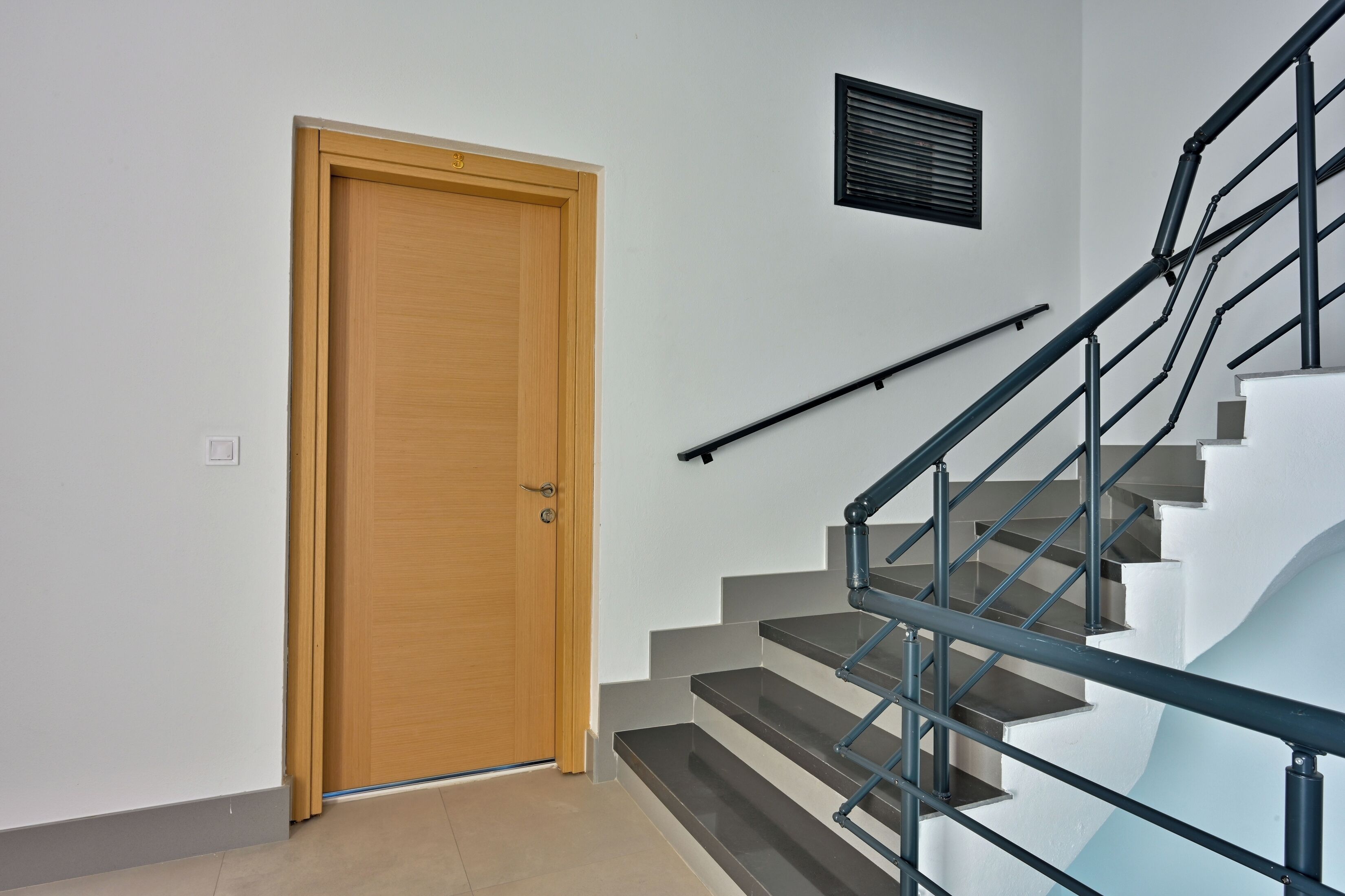 Eine Treppe mit einer Holztür und einem Wandlüfter.