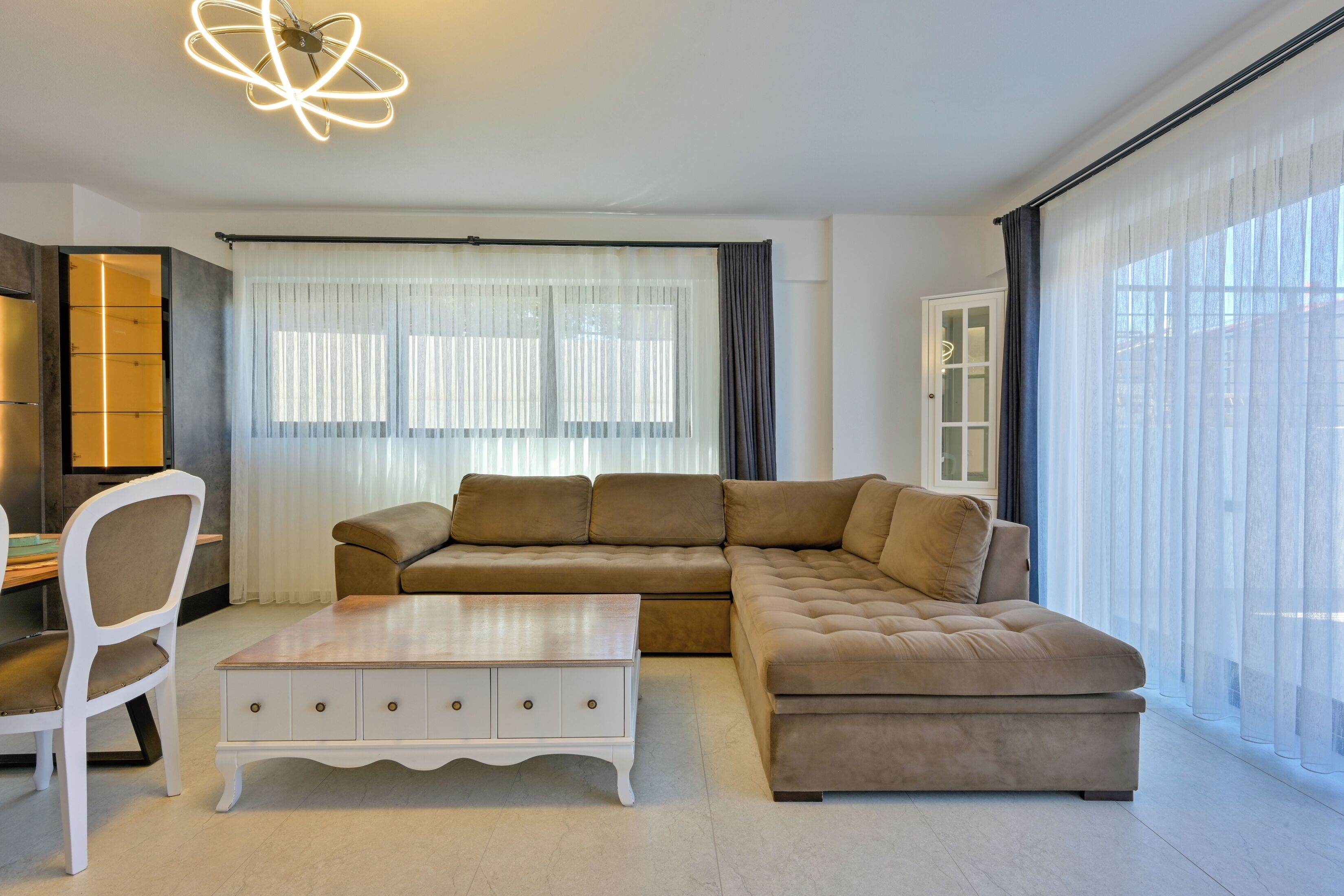 Een moderne woonkamer met een hoekbank, een witte salontafel en een eethoek met een stoel en tafel.