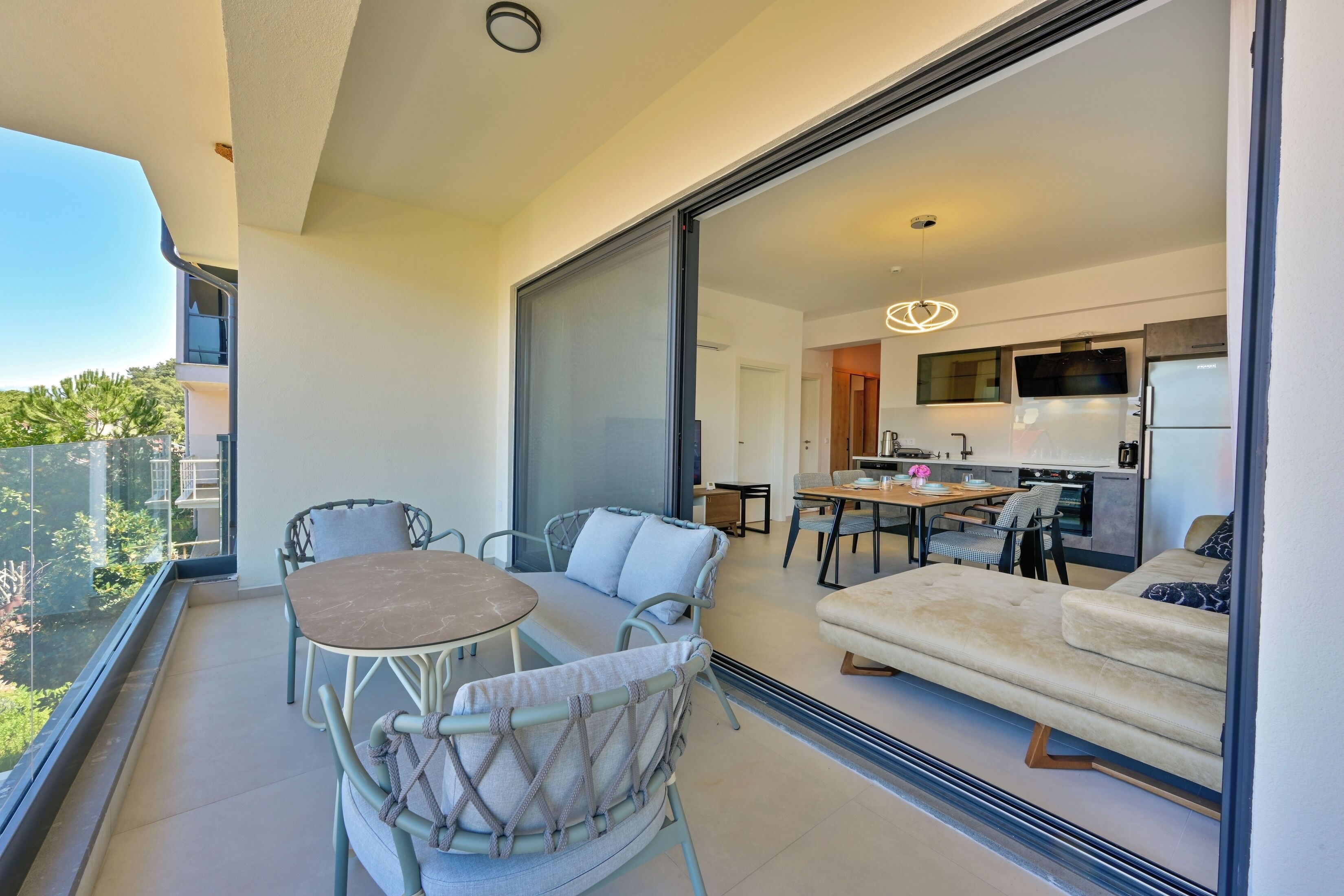 A balcony with a dining table and chairs, a sofa, and a kitchen visible through a glass door.