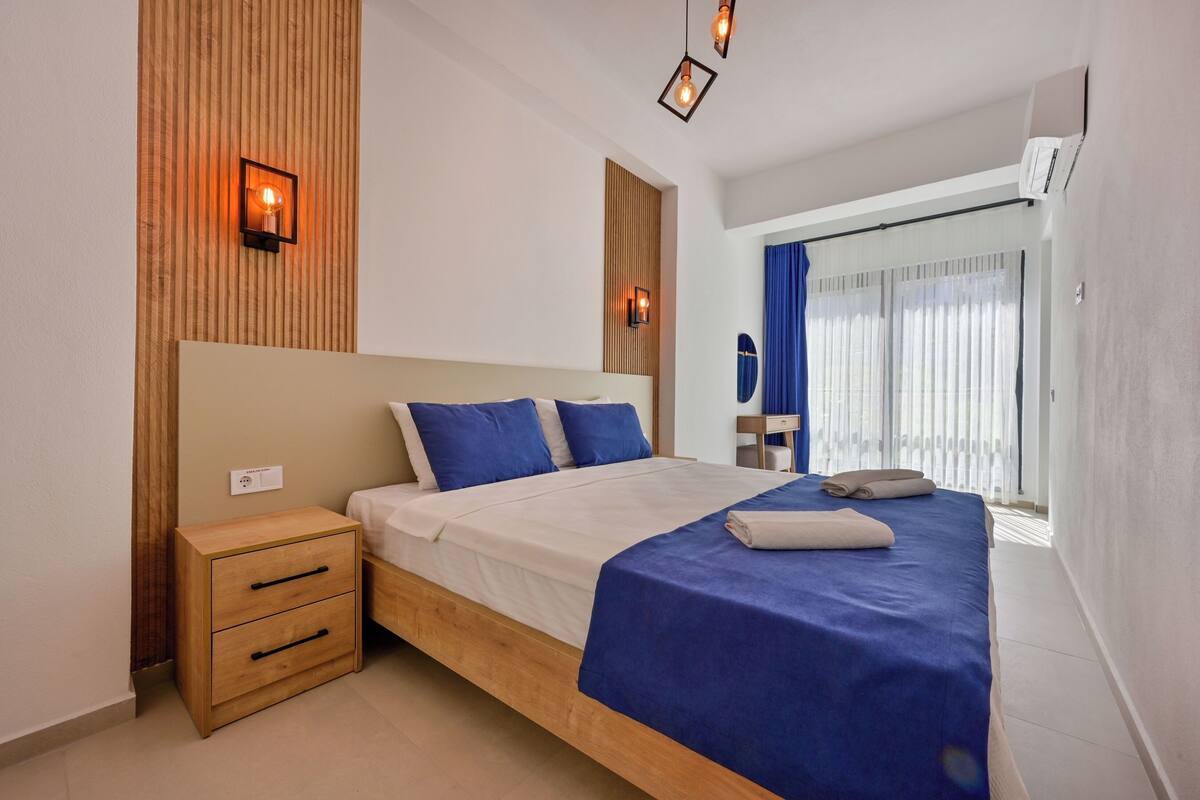 A modern bedroom with a wooden headboard, a single bed with blue bedding, a wooden nightstand, and two wall-mounted lights.