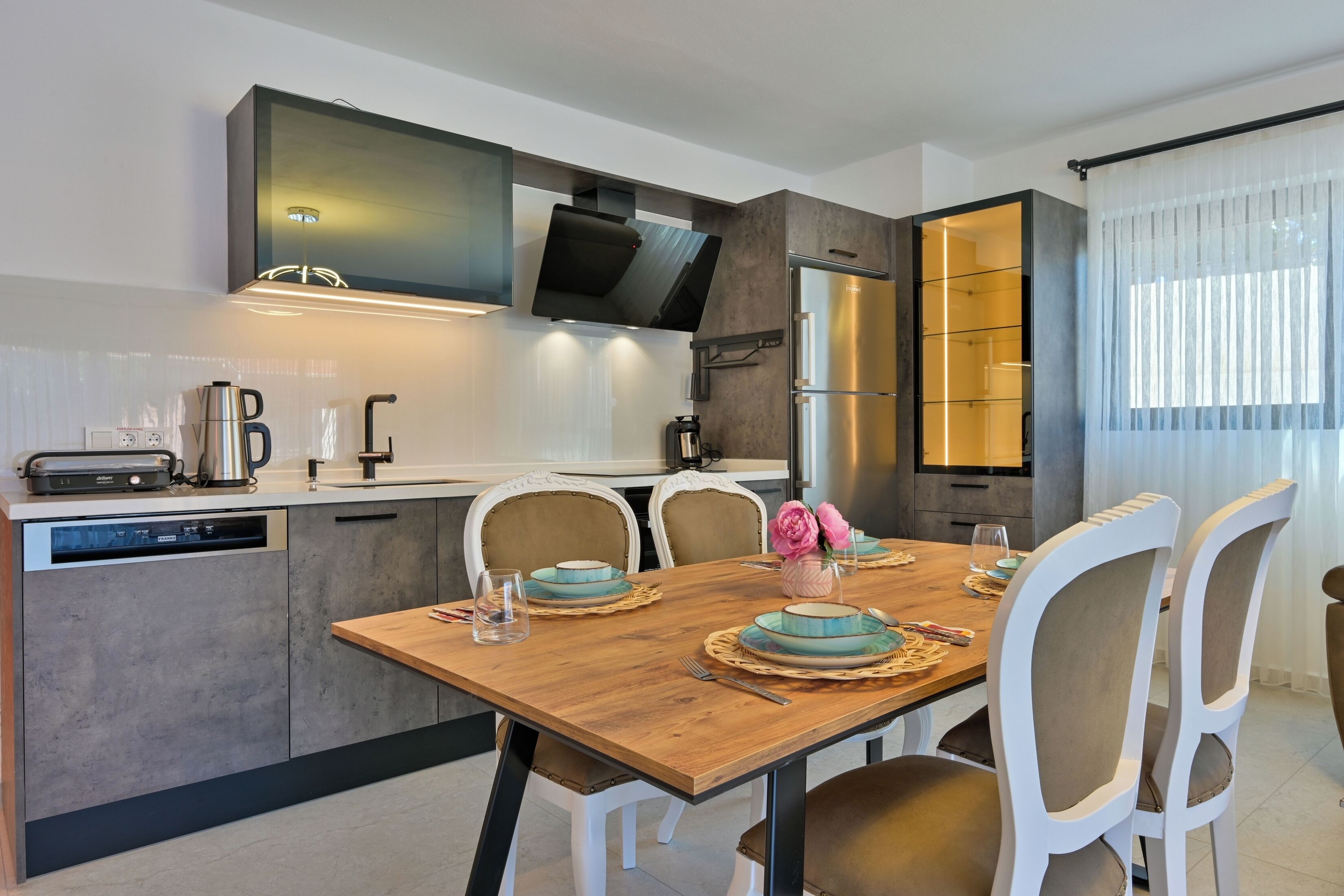 Une cuisine moderne avec une table à manger en bois, des chaises blanches et des appareils électroménagers intégrés.