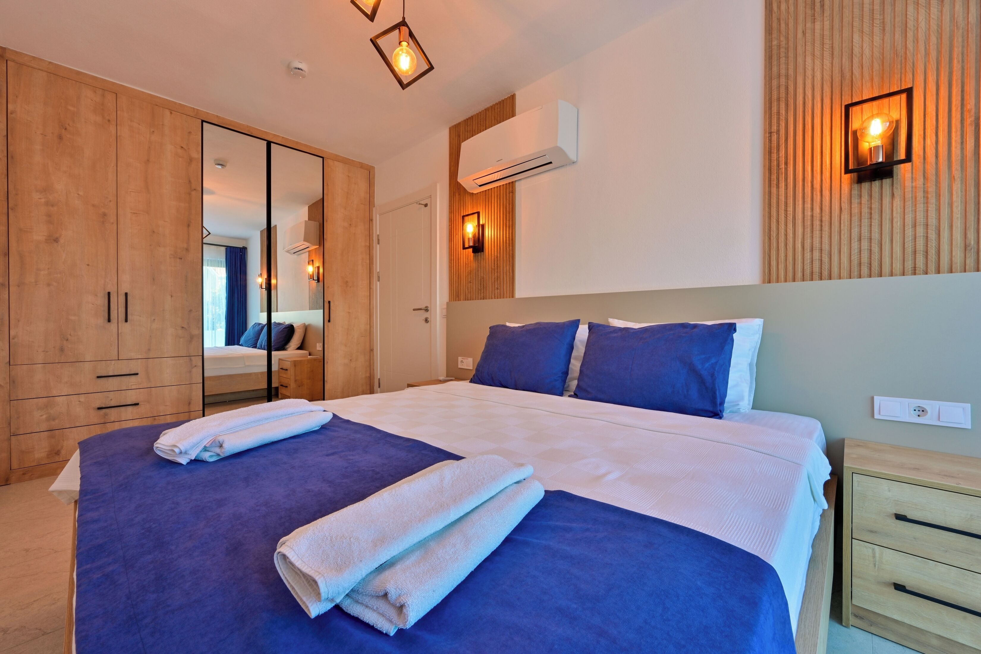 A modern bedroom with a large bed, wooden wardrobe, and a mirror.