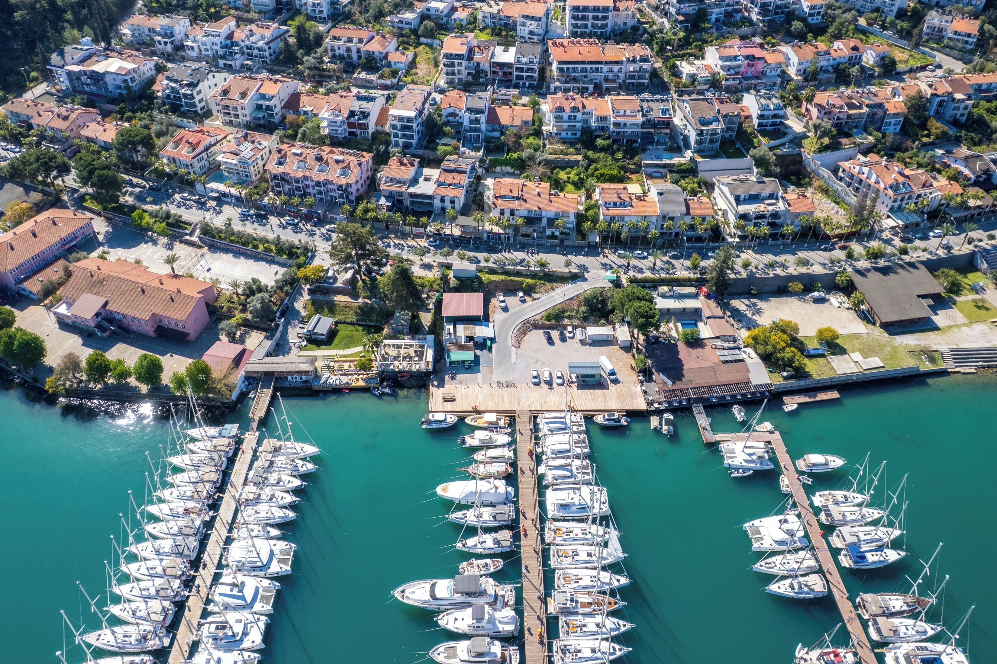 An aerial view of a marina with numerous boats docked, surrounded by residential buildings and a small pier.
