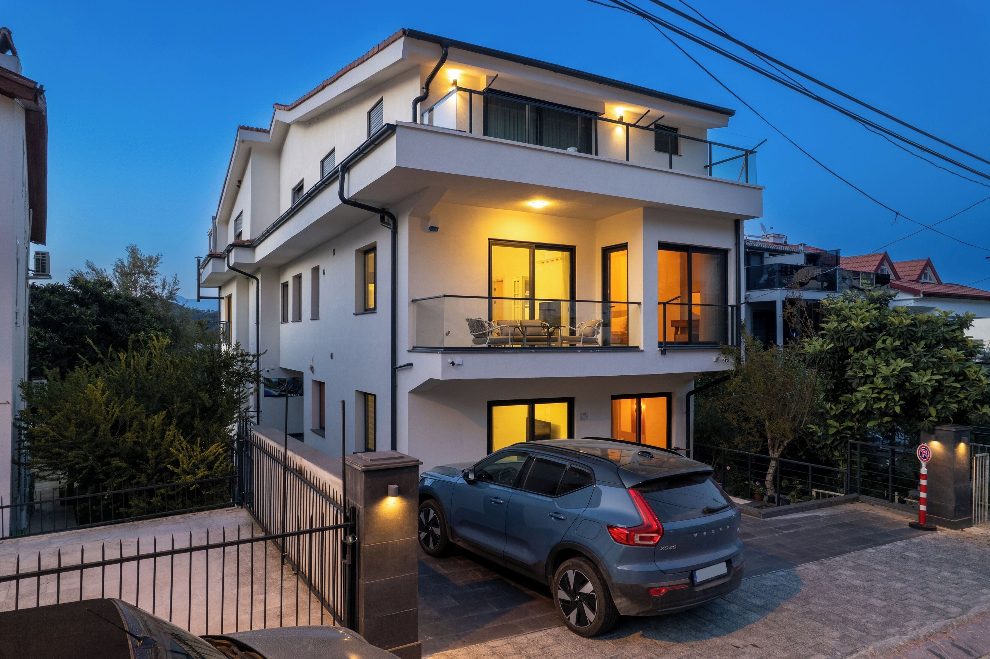 Une maison moderne à deux étages, dotée d’un balcon, avec une voiture garée devant et un ciel dégagé.