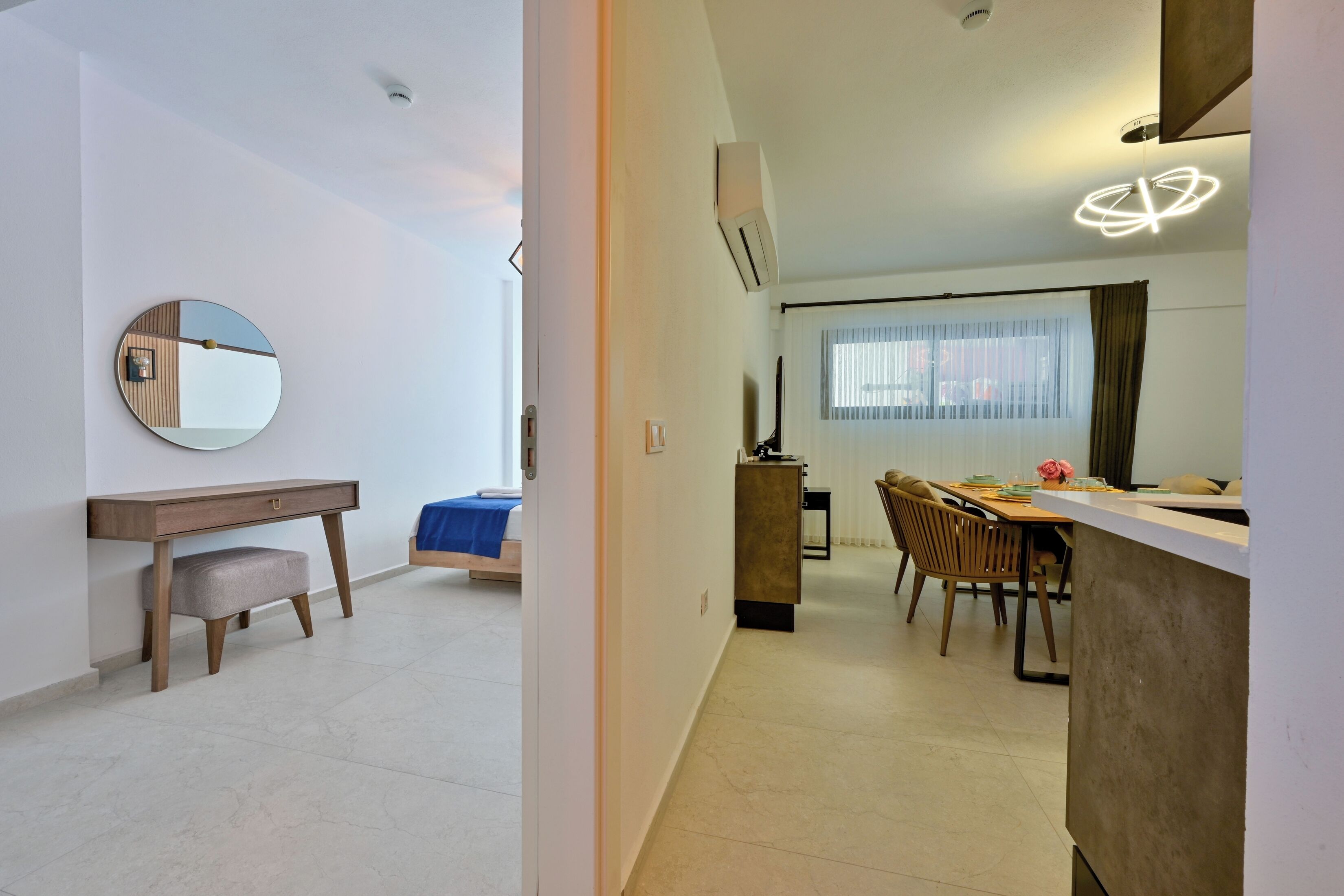 Ein modernes Wohnzimmer mit Essbereich, einem runden Spiegel, einem Holztisch und einem Bett mit blauer Bettdecke.