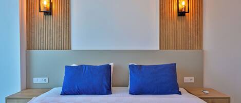 A neatly made double bed with two blue pillows, a wooden headboard, and two wall-mounted lights.