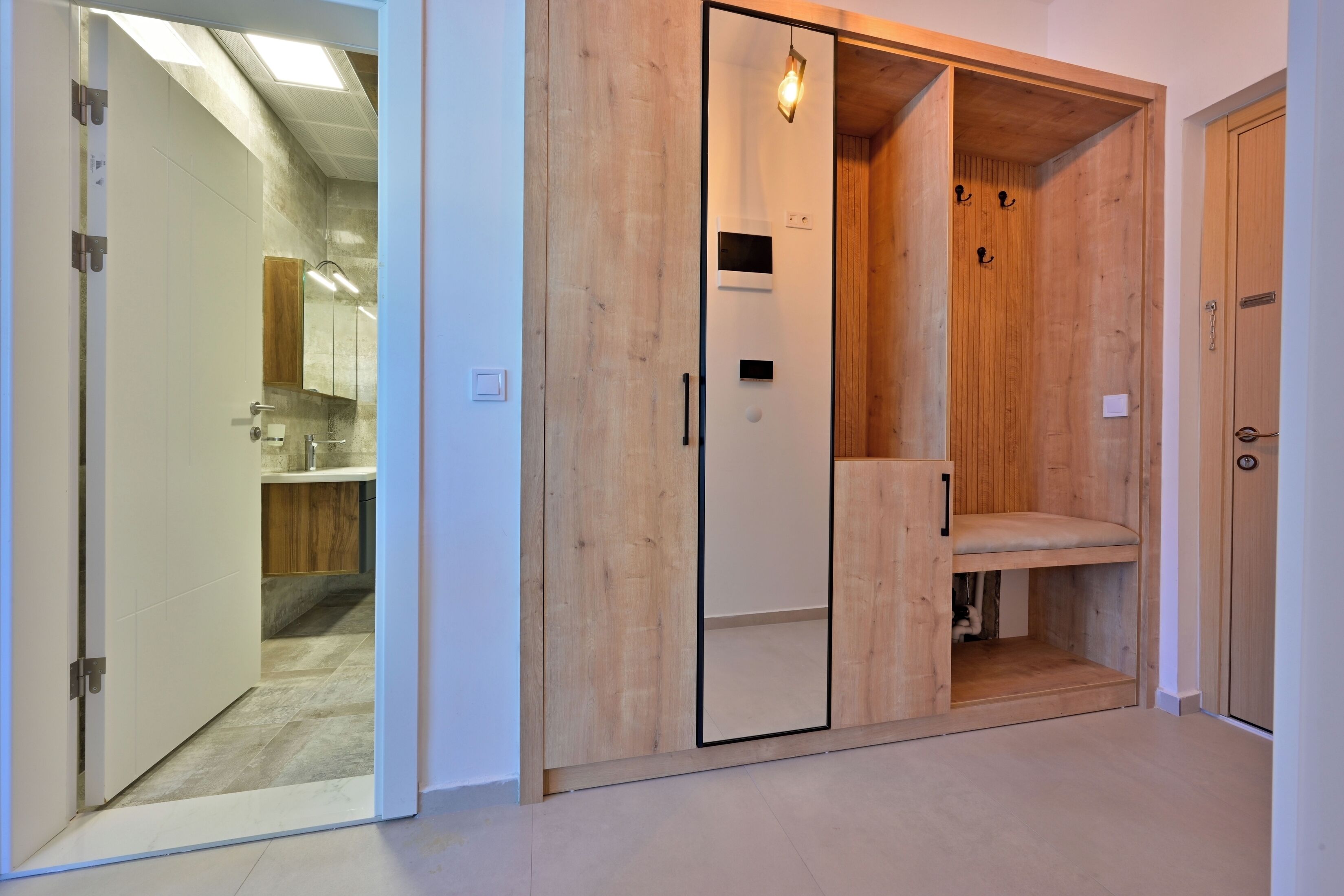 A room with a wooden wardrobe, a door leading to a bathroom, and a small shelf.