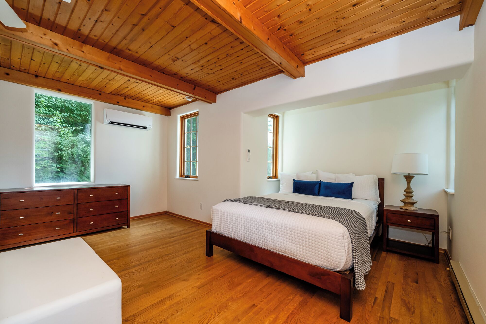 Une chambre avec un plafond en bois, un grand lit avec une literie blanche, une table de chevet avec une lampe et une commode.