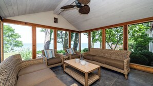 A sunroom with wicker furniture, a ceiling fan, and a view of the sea. - (3 Nt Min) Lakefront Stunner Has It All! (Stevensville)