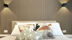 Un dormitorio con pared de listones de madera, cama con almohadas estampadas y dos lámparas fijadas a la pared.