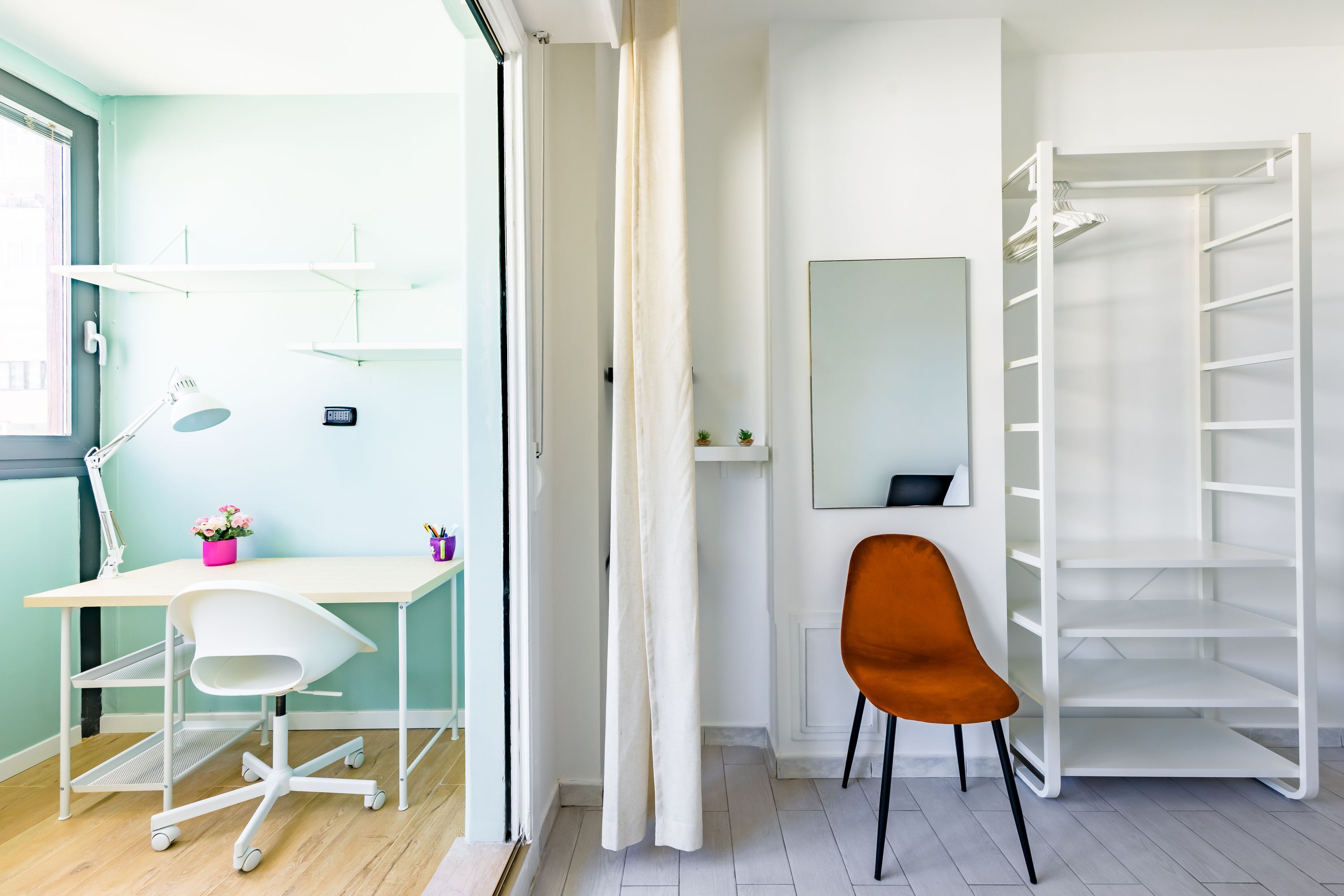 Een kamer met een wit bureau, een stoel, een spiegel en een witte plank.