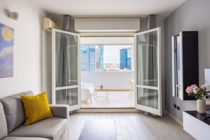 A modern living room with a grey sofa, a yellow cushion, and a glass door leading to an outdoor balcony with a city view. - Casa Kenzo With Parking by Napoliapartments (Naples)