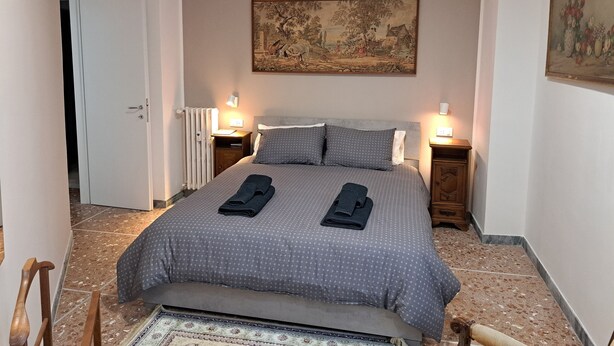 A bedroom with a bed, two bedside tables with lamps, a radiator, and a painting on the wall.