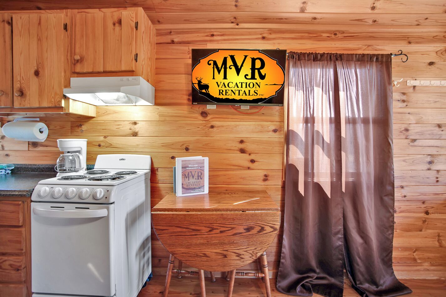 Cocina de cabaña de madera con estufa, cafetera y un cartel de MVR Vacation Rentals.
