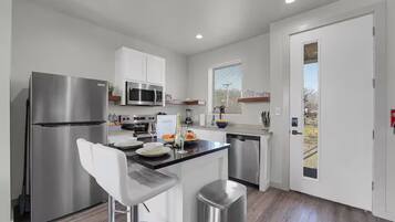 A modern kitchen with stainless steel appliances, a bar stool, and a view of the outdoors.