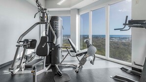 A gym with various exercise machines, a weight stack, and a view of the outdoors through large windows. - 🌴Lighthouse 914: Beachfront Condo w/ Large Balcony & Gulf Views🌴 (Gulf Shores)