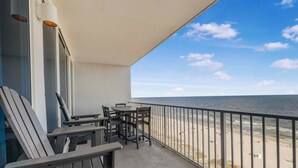 A balcony with a view of the beach, featuring a table and chairs, and a railing. - 🌴Lighthouse 914: Beachfront Condo w/ Large Balcony & Gulf Views🌴 (Gulf Shores)