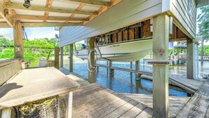 Une terrasse en bois couverte, avec un bateau amarré en dessous, une table et un filet de pêche.
