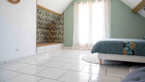 A bedroom with a sloped ceiling, a bed with a patterned bedspread, a window with sheer curtains, and a wall with a decorative lattice.