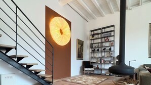 A modern interior with a staircase, a large wall-mounted light, a bookshelf, and a fireplace.
