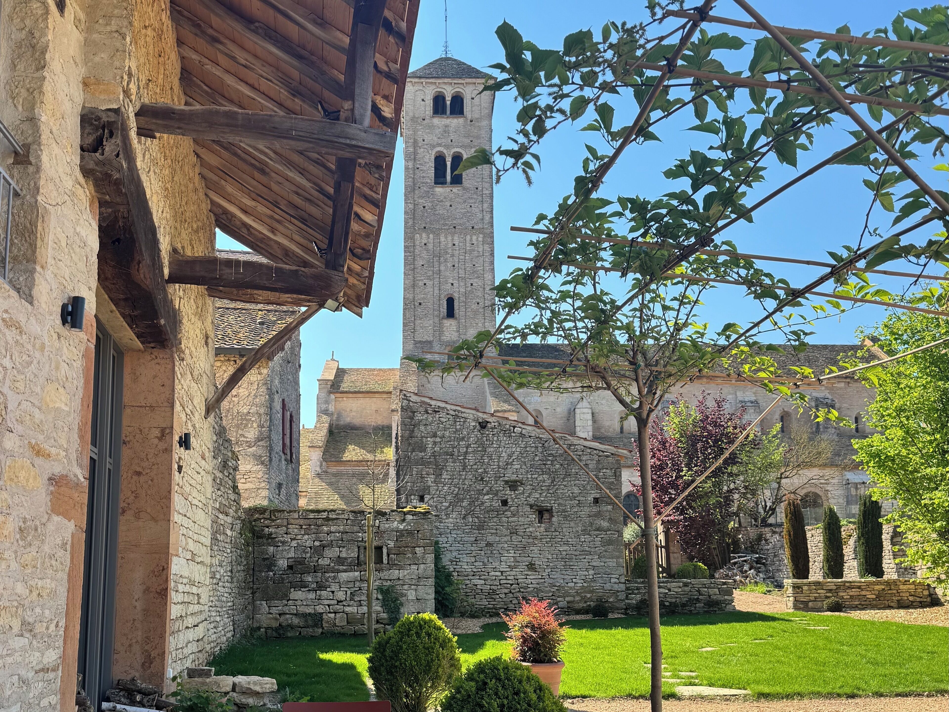 A stone building with a tower, surrounded by a well-maintained garden and a wooden structure.
