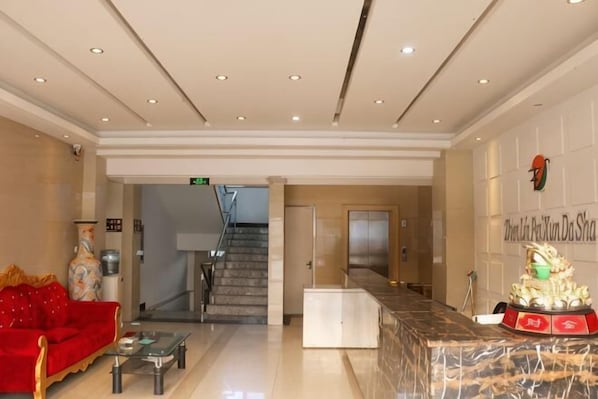 A hotel lobby with a reception desk, a staircase, a red sofa, and a statue.