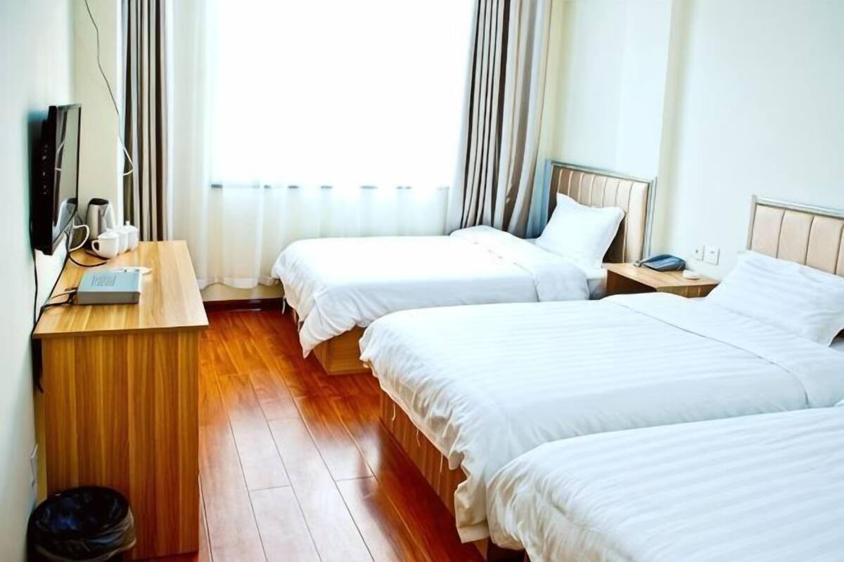 A hotel room with two beds, a wooden desk, a TV, and a window with curtains.