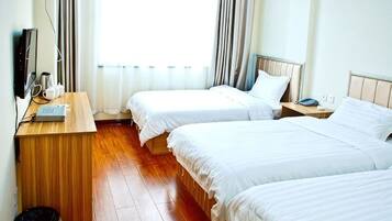 A hotel room with two beds, a wooden desk, a TV, and a window with curtains.
