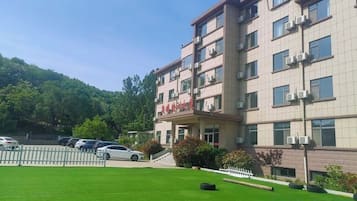 A multi-story building with a flat roof, a parking area, and a well-maintained lawn.