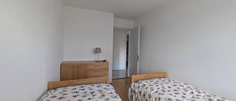 Un dormitorio con dos camas, un aparador de madera y una puerta que da a otra habitación.