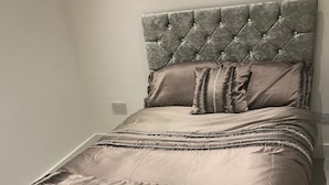 Un lit doté d’une tête de lit capitonnée, d’une couvre-lit à motifs et d’un pied de lit décoratif.