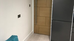 Une chambre moderne avec un canapé de couleur turquoise, une armoire en bois et un réfrigérateur noir.