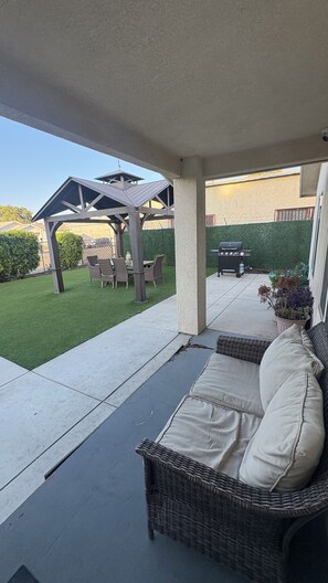 A covered patio area with a wicker sofa, a grill, and a dining set.