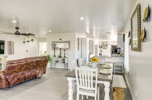 A spacious living area with a brown leather sofa, white dining table, and chairs.