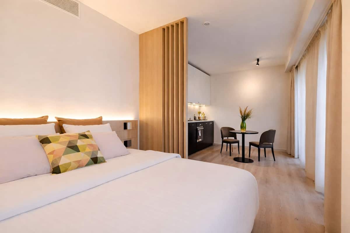 Una camera d'albergo con un letto grande, una scrivania con una sedia, un tavolino con un vaso e un angolo cottura.
