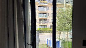 A room with a sliding glass door leading to a balcony with a view of a residential building and a parked blue vehicle. - Stay at Brussels (Brussels)
