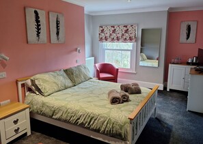 A bedroom with a bed, a red chair, a desk, and a window with a floral blind. - Room-comfortable Double Room With Bath (Cranleigh)