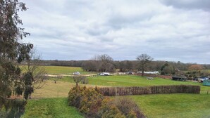 Paisaje rural con campos abiertos, algunos árboles y una vista distante de un pequeño asentamiento con edificios y vehículos.