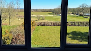 A view through a window of a rural landscape with fields, trees, and a distant building.