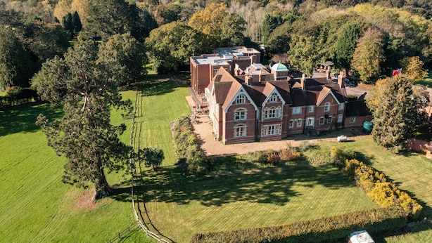 A large, historic building with multiple chimneys, surrounded by well-maintained lawns and mature trees.