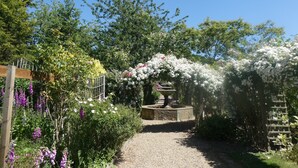 A garden pathway with a gravel surface, surrounded by various flowering plants and trees.