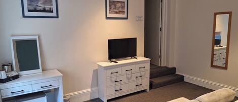 A bedroom with a bed, a desk with a computer, a TV, and two framed pictures on the wall.