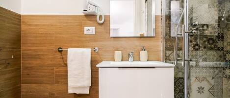 A bathroom with a wooden wall, a white sink, a mirror, a towel rack, a hairdryer, and a shower with patterned tiles.